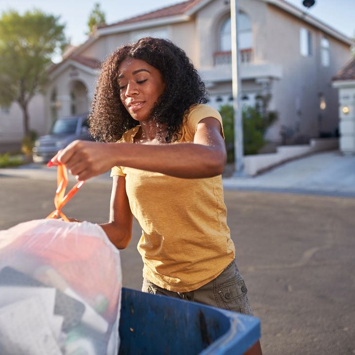 An african american woman taking out the trash in a desert neighborhood.